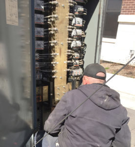 kneeling tech in a grey hoodie looking at exposed wires