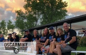 group of adults in america shirts sitting outside smiling with the oscarmike logo in the lower righthand corner